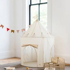 a white teepee tent sitting on top of a wooden floor next to a window