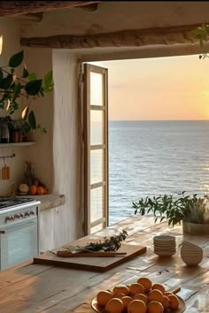 a table with oranges on it in front of an open window overlooking the ocean