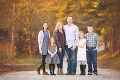 a family posing for a photo in the middle of an autumn forest with leaves on the ground