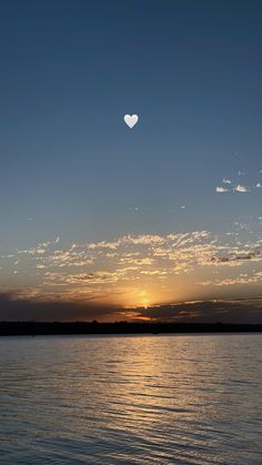 the sun is setting over the water with a heart shaped object in the sky above it