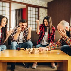 group of people playing board game on wooden table in living room with couch and windows