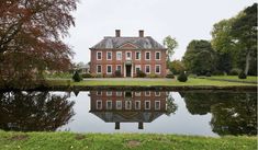 a large red brick house sitting on top of a lush green field next to a lake