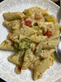 a white plate topped with pasta covered in sauce and veggies next to a spoon