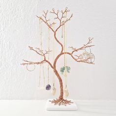 a wire tree with jewelry hanging from it's branches on a white table next to a wall