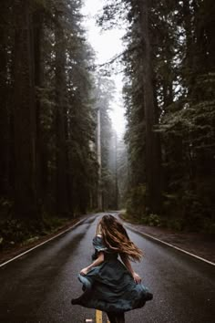 a woman in a blue dress is walking down the road with her hair blowing in the wind