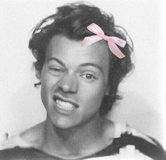 a black and white photo of a man with a pink bow on his head smiling