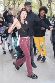 a woman in red pants and black top walking down the street with other people behind her