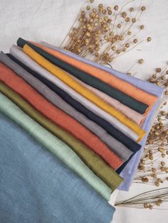 a stack of different colored linens sitting on top of a table next to dried flowers