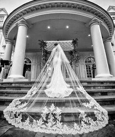 a bride standing in front of a large building with her veil blowing in the wind