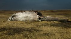 an old airplane sitting in the middle of a dry grass field under a cloudy sky