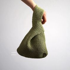 a hand holding a green knitted bag in the air