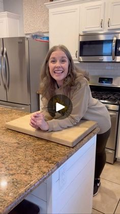 a woman sitting at a kitchen counter with a cutting board on top of the counter