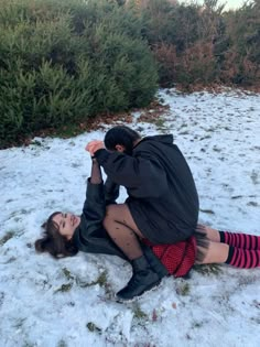 a man and woman sitting in the snow with their hands on each other's shoulders