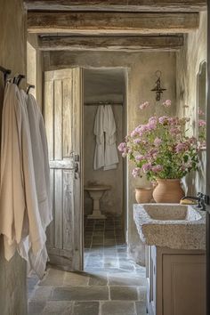 an open door leading to a bathroom with flowers in the sink and towels hanging on hooks