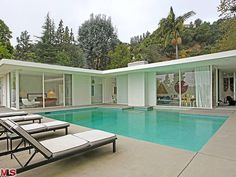 an outdoor swimming pool with chaise lounges next to it and trees in the background