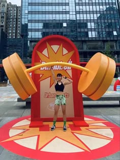 a woman standing in front of a giant sign with two large yellow dumbs on it