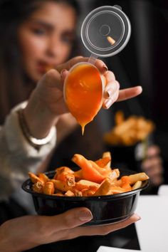 a woman is pouring sauce into a bowl of food that includes french fries and carrots