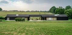 a large black house sitting in the middle of a lush green field with lots of trees