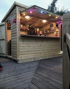 a small wooden bar on a deck with lights hanging from it's roof top