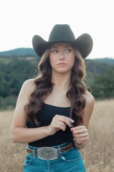 a beautiful young woman wearing a cowboy hat in the middle of an open field with tall grass