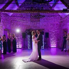 a bride and groom dance on the dance floor at their wedding reception with purple lighting