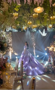 a woman in a purple dress standing next to a table with flowers and candles on it