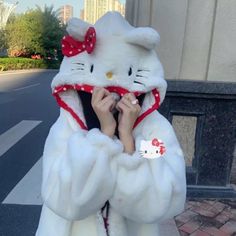 a woman wearing a hello kitty costume and holding her hands to her face while standing on the street