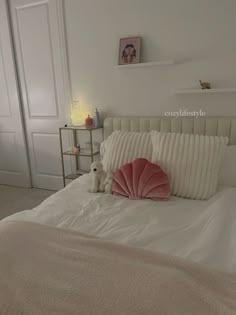 a white bed topped with pillows and a stuffed animal sitting on top of it's side