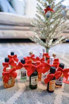 bottles of liquor tied with red ribbon on carpet next to christmas tree in living room