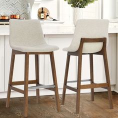 two white bar stools sitting in front of a kitchen counter with flowers on it