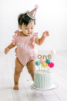 a baby girl standing in front of a cake with one on it and the number one sign