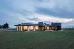 a modern house sits on the edge of a grassy field at dusk with its lights on