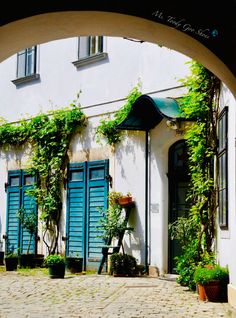 an arch leading into a building with blue shutters and potted plants on the outside