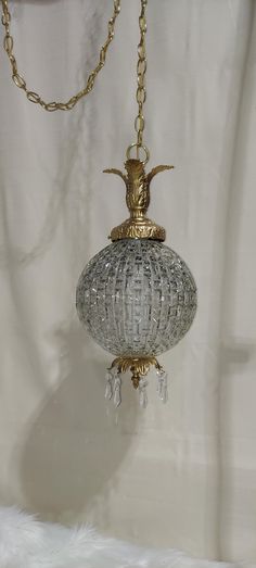 a glass and brass hanging light fixture on a white curtained room with a chain attached to it