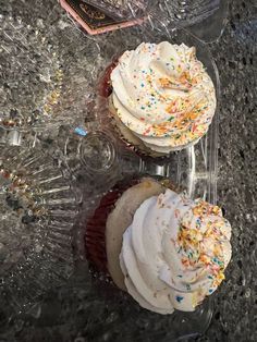 two cupcakes with white frosting and sprinkles on them sitting on a table