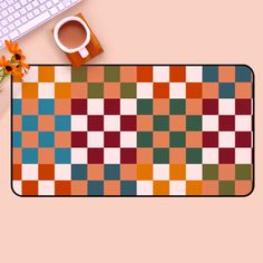 an orange and green checkered rug next to a keyboard, coffee cup and flower