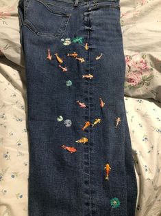 an embroidered pair of jeans with fish on the side and flowers all over them, sitting on a bed