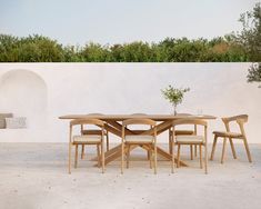 a wooden table and chairs in front of a white wall with an olive tree on it