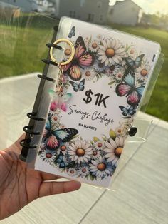 a person holding up a small book with butterflies on it and the words $ 1k