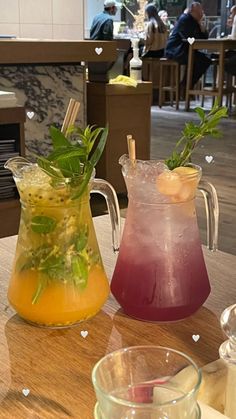 two pitchers filled with drinks sitting on top of a wooden table next to each other