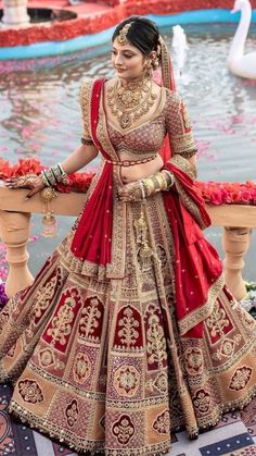 a woman in a red and gold bridal gown standing next to a swan pond