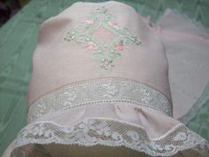 a pink hat with white lace trim and flowers on the side, sitting on a green surface