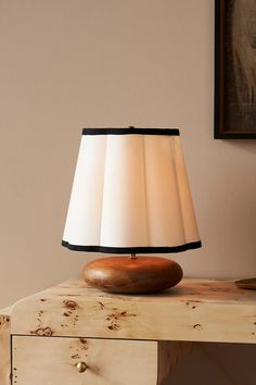 a lamp sitting on top of a wooden table next to a painting and a dresser