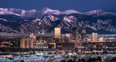 the city is surrounded by mountains and snow covered hills in the distance are lit up at night