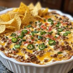 a casserole dish filled with cheese, green peppers and ground beef surrounded by tortilla chips