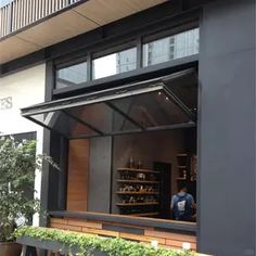 a man standing in the window of a coffee shop with plants growing on the outside