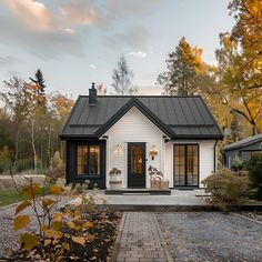 a small white house with a black roof and brick walkway leading to the front door