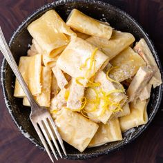 a bowl filled with pasta and cheese on top of a wooden table next to a fork