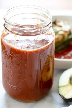 a glass jar filled with ketchup next to an avocado