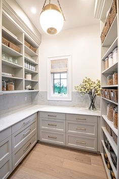 a white kitchen with lots of shelves and drawers on the wall, along with a vase filled with flowers